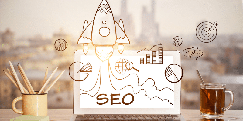 Laptop displaying SEO strategy sketches with a rocket launching, surrounded by business icons.